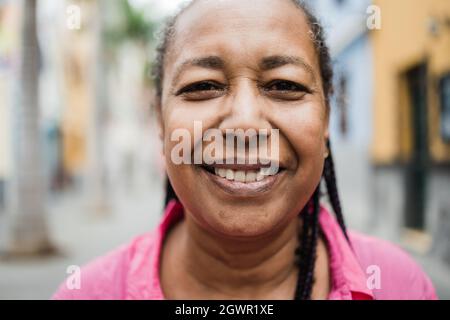 Glückliche ältere afrikanische Frau posiert und lächelt vor der Kamera mit Stadt im Hintergrund - echte Menschen, Vielfalt und ältere Menschen Konzept - Fokus auf Augen Stockfoto