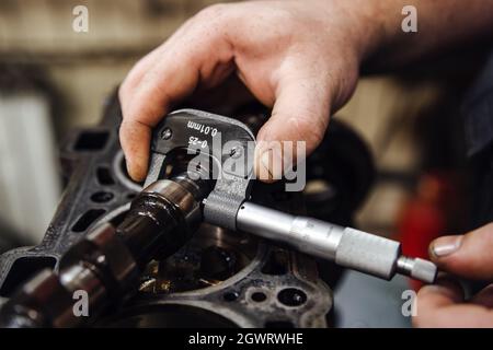 Ein Messgerät in der Hand misst die Nockenwelle vor dem Hintergrund eines Motors in geringer Schärfentiefe Stockfoto