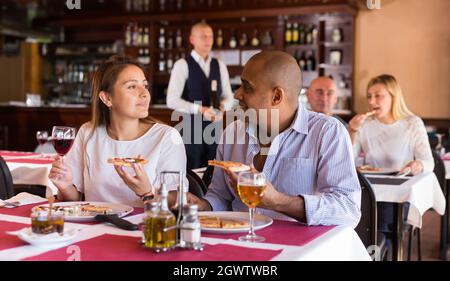 Positives lateinamerikanisches Paar, das im Restaurant Pizza isst Stockfoto