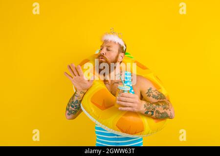 Mann mit Rettungsboje und Prinzessin Krone trinkt einen Fruchtsaft Stockfoto