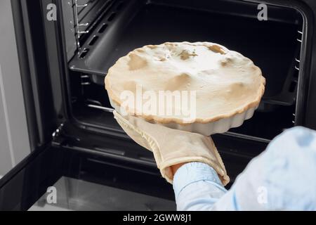 Frau, die ungekochte Hühnertopf-Pie mit Gemüse in den Ofen legte Stockfoto