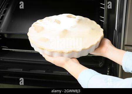 Frau, die ungekochte Hühnertopf-Pie mit Gemüse in den Ofen legte Stockfoto