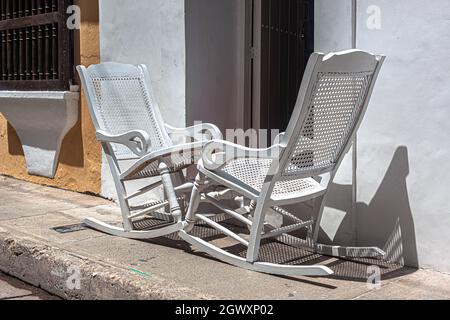 Zwei hölzerne Schaukelstühle auf einem Bürgersteig, direkt vor einem republikanischen Kolonialhaus, Cartagena de Indias, Kolumbien. Stockfoto