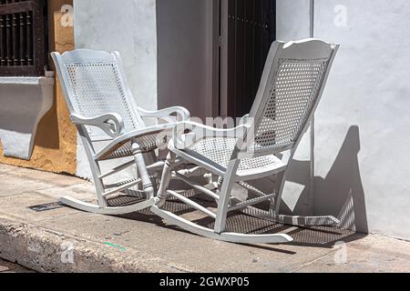 Zwei hölzerne Schaukelstühle auf einem Bürgersteig, direkt vor einem republikanischen Kolonialhaus, Cartagena de Indias, Kolumbien. Stockfoto