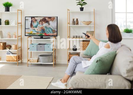 Frau, die zu Hause auf dem Sofa sitzt und ihren Fernseher mit großem Bildschirm anschaltet Stockfoto