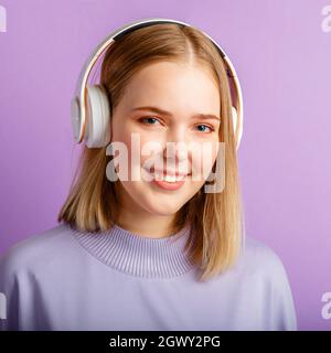 Glückliche junge Frau im Headphones-Portrait. Schöne lächelnde Frau mit blonden Frisuren genießen Sie Musik in Kopfhörer über lila isoliert hören Stockfoto