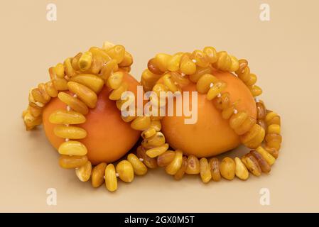 Wunderschöne Bernsteinperlen, zwei Kaki und ein kleines Glas Rum auf natürlichem Hintergrund. Komposition „Goldener Herbst“ Stockfoto