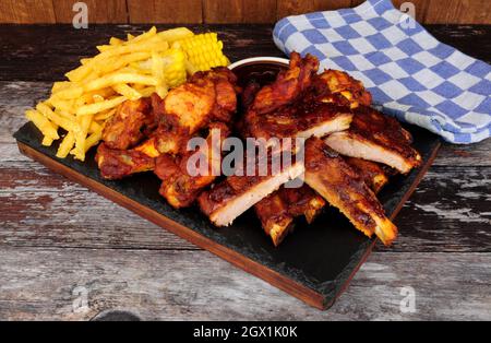 Grillen Sie Schweineribs und Hähnchenflügel mit Pommes frites und Mais auf dem Maiskolben Stockfoto