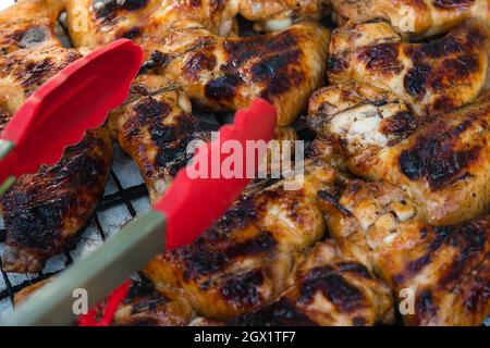 Nahaufnahme von gegrillten Hähnchenflügeln und roten Küchenzangen. Selektiver Fokus. Das Konzept des Kochens im Hinterhof Stockfoto