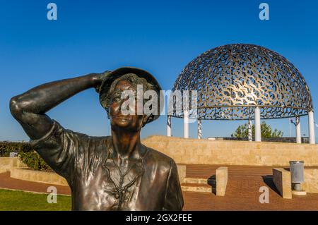 Am Abend hielt die bronzene Statue einer Frau ihren Hut in der Meeresbrise mit Blick auf den Geraldton Hafen an der HMAS Sydney 11-Gedenkstätte. Stockfoto