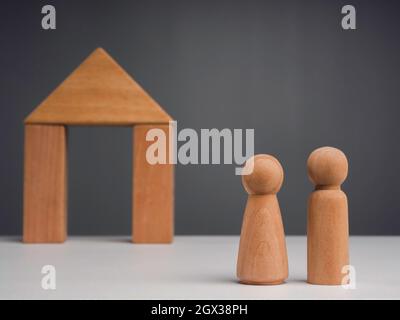 Ein Paar beginnt ein Leben zusammen mit dem Immobilieninvestitionskonzept. Das hölzerne Menschenpaar, das vor einer Holzhausminiatur steht Stockfoto
