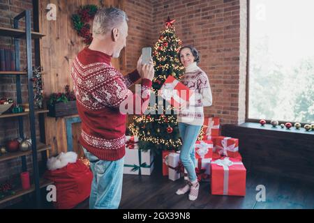 Fotoporträt älteres Paar, das zusammen mit weihnachtsgeschenken in dekorierten Wohnungen fotografiert Stockfoto
