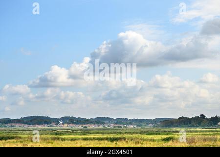 Blick auf Cley neben dem Sea Village von der Wanderroute in Blakeney Freshes mit großem, blauem Himmel und flauschigen weißen Wolken, Norfolk, England. Stockfoto