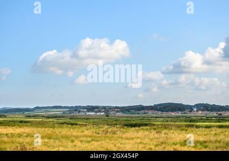 Blick auf Cley neben dem Sea Village von der Wanderroute in Blakeney Freshes mit großem, blauem Himmel und flauschigen weißen Wolken, Norfolk, England. Stockfoto