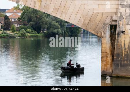 Ein Fischer in seiner Bootsanlegestelle, der auf dem Fluss Saone unter der Saint Laurent-Brücke in Chalon Sur Saone, Frankreich, fischt. Stockfoto