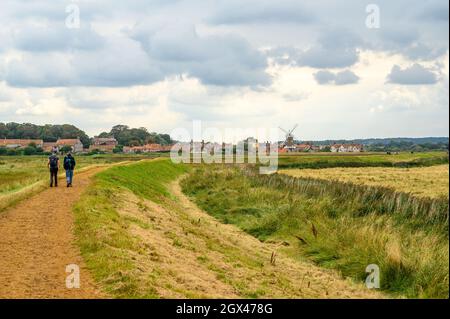 Menschen, die auf dem Blakeney Freshes Rundwanderweg in Richtung Cley on the Sea Village mit seiner Windmühle, Norfolk, England, wandern. Stockfoto