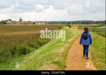 Menschen, die auf dem Blakeney Freshes Rundwanderweg mit Blick auf das Dorf Cley on the Sea mit seiner Windmühle, Norfolk, England, wandern. Stockfoto