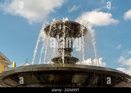 Wasser strömt aus einer Schale aus schwarzem Marmorbrunnen an einen blauen Himmel mit kleinen Wolken. Stockfoto