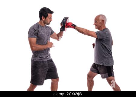 Älterer Mann schlägt mit Boxhandschuh in der Verteidigung, persönliche Fitness-Trainer, Konzept der Zusammenarbeit. Auf weißem Hintergrund. Stockfoto