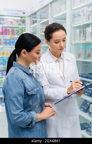 Apotheker schreibt auf Zwischenablage in der Nähe von asiatischen Frau in der Drogerie Stockfoto