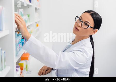 asiatischer Apotheker in Gläsern, der in der Drogerie Medikamente erreicht Stockfoto