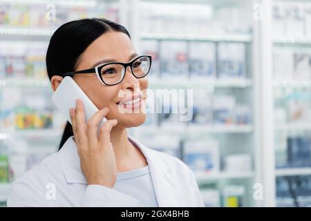 Fröhlicher asiatischer Apotheker in Brille im Gespräch auf dem Smartphone Stockfoto