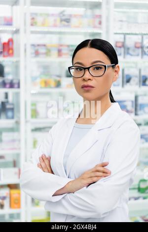 asiatischer Apotheker in einer Brille, die in der Drogerie mit gekreuzten Armen steht Stockfoto