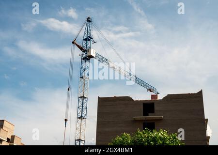 An einem Sommertag erhebt sich ein Turmkran über einem im Bau befindlichen Backsteinhaus gegen den Himmel. Stockfoto