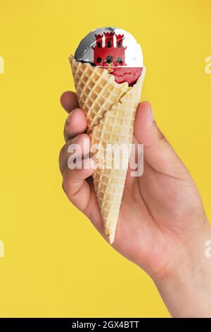 Auf einem farbenfrohen Hintergrund eine Hand mit Eis in Form der Flagge von Gibraltar Stockfoto
