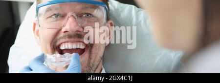 Der Arzt versucht, einen Mundschutz aus Kunststoff zu nutzen, damit ein junger lächelnder Mann den Bissen korrigieren kann Stockfoto