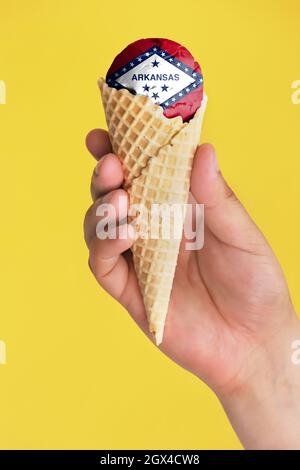 Auf einem farbenfrohen Hintergrund eine Hand mit Eis in Form der Flagge des Staates Arkansas Stockfoto