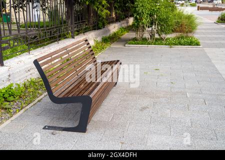 Auf dem Asphalt steht neben einem Metallzaun eine interessant gestaltete Straßenbank. Stockfoto