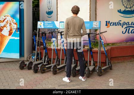 Ein junger Mann steht an der Theke von Elektro-Scootern für mobile Bewegung in der Stadt und liest die Mietregeln in russischer Sprache. Stockfoto