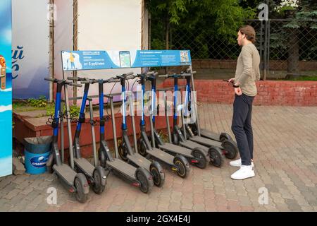 Ein Typ steht an einer Theke mit Elektrorollern für die mobile Bewegung in der Stadt und liest die Mietregeln in russischer Sprache. Stockfoto