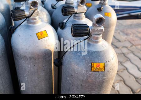 Viele Alu-Tauchsauerstofftanks stehen vor den grünen Strandbüschen und Felsen auf dem Sand in Thailand mit Kopierraum Stockfoto
