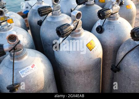 Viele Alu-Tauchsauerstofftanks stehen vor den grünen Strandbüschen und Felsen auf dem Sand in Thailand mit Kopierraum Stockfoto