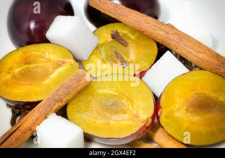 Hälften von Pflaumen, Zimtstangen, Zuckerwürfeln und Nelken Stockfoto