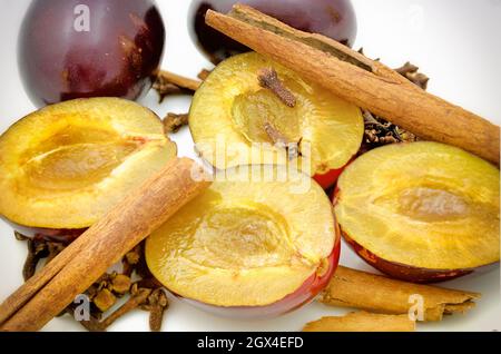 Hälften von saftigen Pflaumen, Zimtstangen und Nelken Stockfoto