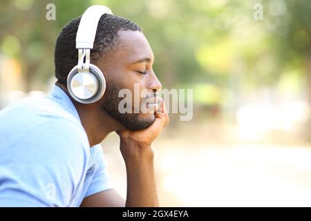 Profil eines schwarzen Mannes, der in einem Park mit kabellosen Kopfhörern Musik hört Stockfoto
