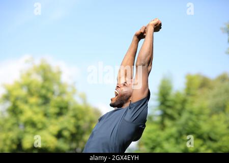 Seitenansicht Porträt eines aufgeregten schwarzen Mannes, der in einem Park die Arme hebt Stockfoto