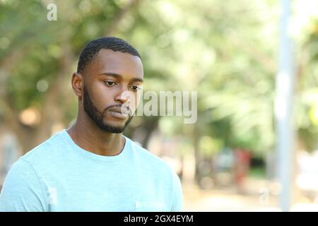 Trauriger schwarzer Mann, der wegschaute, abgelenkt in einem Park spazieren ging Stockfoto