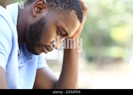 Profil eines besorgten schwarzen Mannes, der sich allein in einem Park beschwert Stockfoto