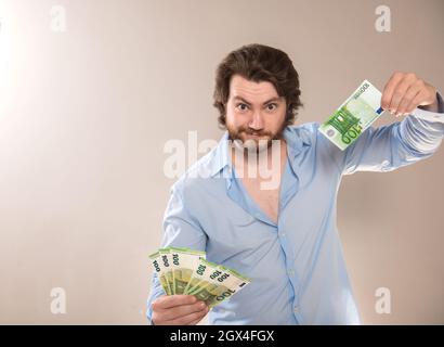 Ein frivol reicher junger Mann hält 100-Euro-Banknoten in den Händen und blickt trotzig auf die Kamera Stockfoto