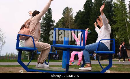 Großmutter, Mutter und Enkelin reiten auf dem Karussell und haben Spaß an einem sonnigen Sommertag. Elternkonzept, Generationenbeziehung, glücklich Stockfoto