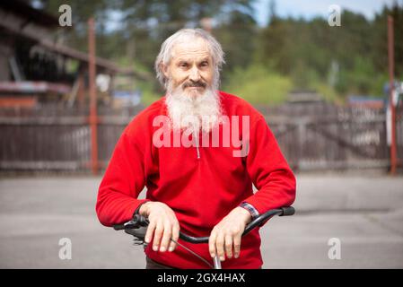 Ein alter Mann mit einem grauen Bart, der auf dem Lenker eines Fahrrads ruht Stockfoto