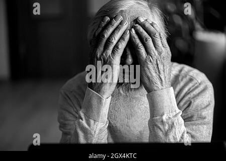 Ein müder, gebrochener, resigniert, beschäftigt älterer Mann sitzt vor einem Laptop, Computer und bedeckt sein Gesicht mit der Hand. Stockfoto