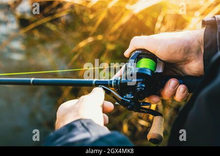 Angelrute mit Multiplikator Haspel und grüne geflochtene Linie in Angler Hände. Nahaufnahme Stockfoto