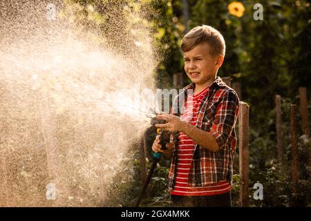 Der kleine Junge wäscht die Pflanzen und macht große Wasserspritzer Stockfoto