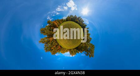 Kleine Planetenprojektion von 360 mal 180 Grad kugelförmigem Panorama von sonniger herbstlicher gemähter Wiese und gelbem Wald an seinen Rändern mit blauem Himmel und Wolke Stockfoto