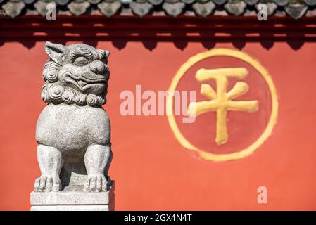 Chengdu, Provinz Sichuan, China - 28. September 2021 : Skulptur des Drachensohns vor der roten Umfassungwand des buddhistischen Klosters Wenshu mit dem chinesischen Schriftzeichen - Ping- was Frieden bedeutet. Stockfoto